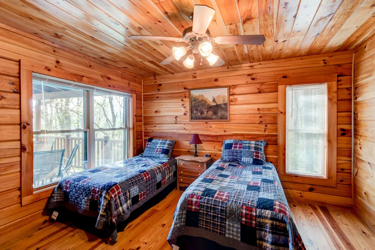 A warm bedroom with two single beds, a large window offering morning sunlight, wooden ceiling, and playful wall art. The inviting atmosphere is perfect for children or friends sharing a private space, as described in the section.