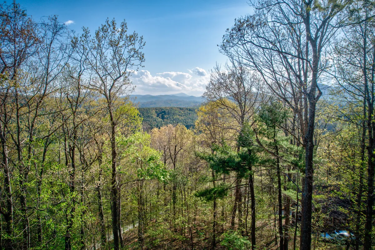 A sweeping view of distant mountains, lush green foliage, and a broad sky filled with clouds. The perspective suggests a vantage point where guests can appreciate breathtaking sunrises or sunsets, with a sense of peace and awe-inspiring natural beauty.