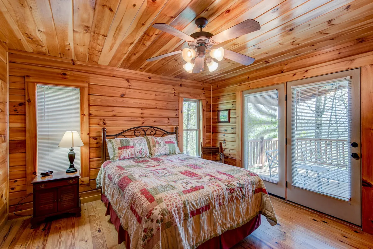 A peaceful bedroom with a bed dressed in a patchwork quilt, wooden ceiling, and ample natural light streaming through the windows. The serene setting suggests a restful escape for couples or guests.