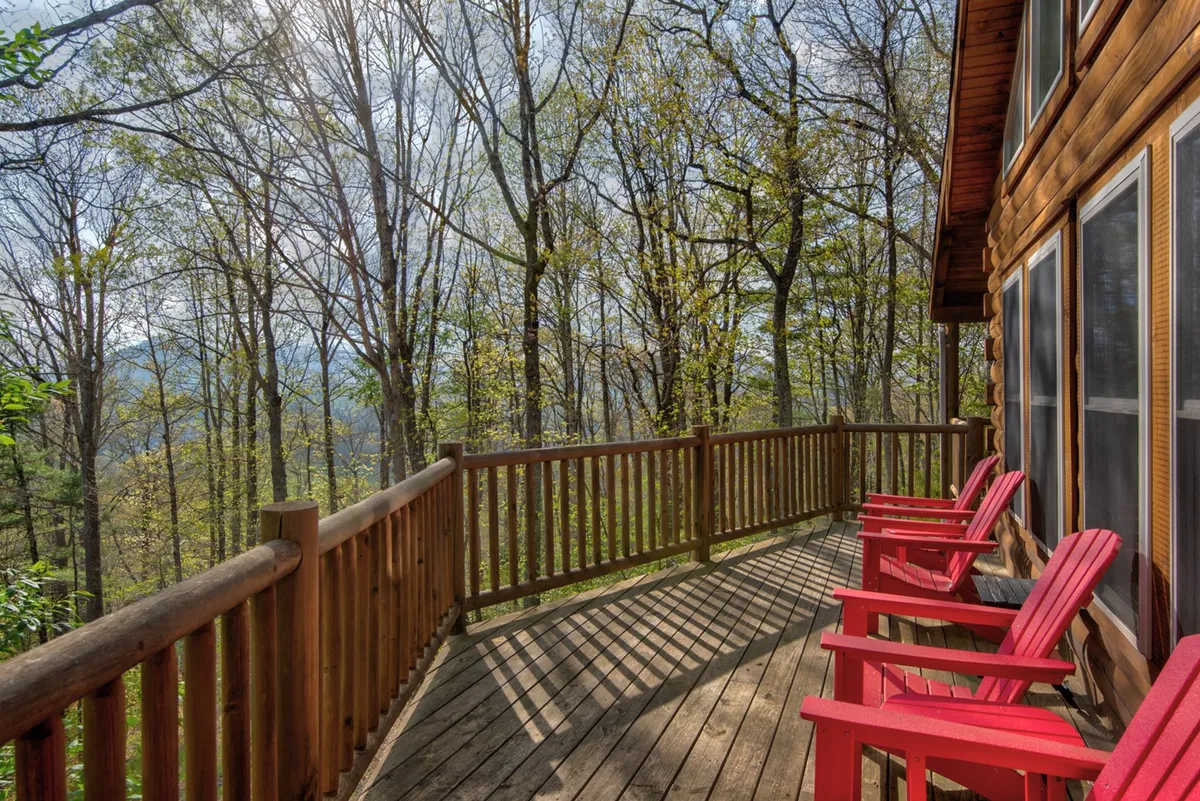An inviting exterior image showcasing a cozy deck with red chairs overlooking natural greenery. This tranquil setting is ideal for sharing stories by the fire, enjoying wildlife, or simply soaking in the peaceful mountain environment after a busy day outdoors.