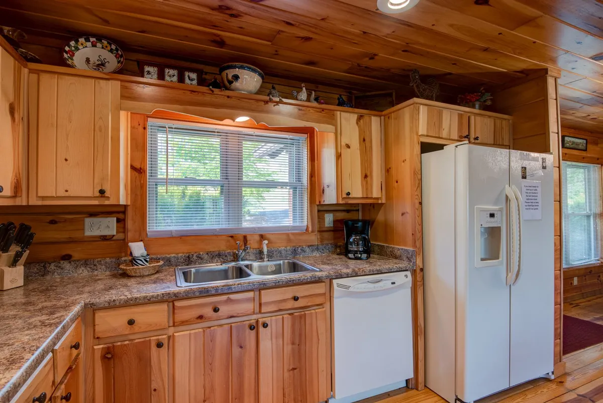 A welcoming kitchen scene featuring wooden cabinetry, a modern refrigerator, kitchen sink, and a window bringing in natural light. The setup encourages cooking, gathering, and making memories over shared meals.