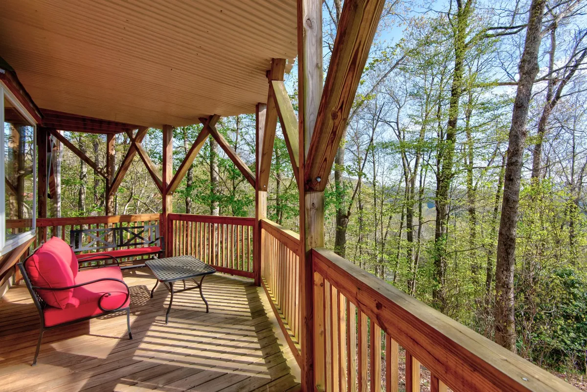 A peaceful exterior shot featuring a red chair and black metal table on a wooden deck, bordered by a rustic railing and surrounded by vibrant greenery. The scene evokes relaxation after a day of adventure, with ample space to enjoy morning coffee or evening stargazing in a serene outdoor setting.