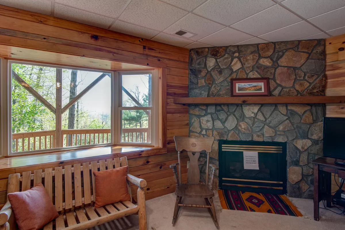A cozy living space featuring a stone fireplace, large window with a scenic view, a wooden bench, and a decorative rug. The atmosphere is inviting, ideal for movie nights or relaxing downtime after games.