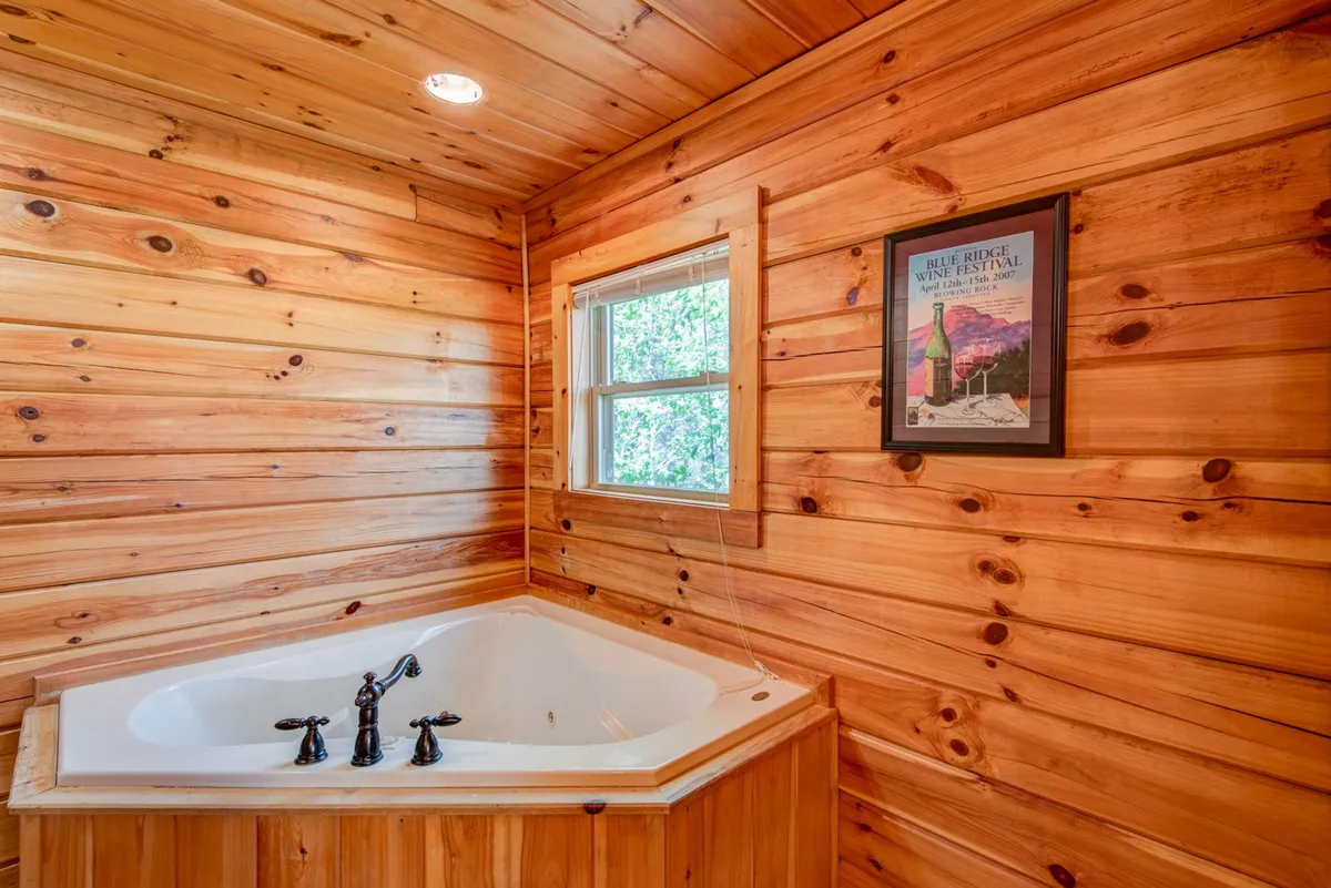 A spacious bathroom featuring a jacuzzi tub set against rustic wooden walls, with a window that lets in natural light and framed artwork adding charm. The tranquil atmosphere is ideal for relaxation, directly echoing the double jacuzzi tub and spa-like amenities described.