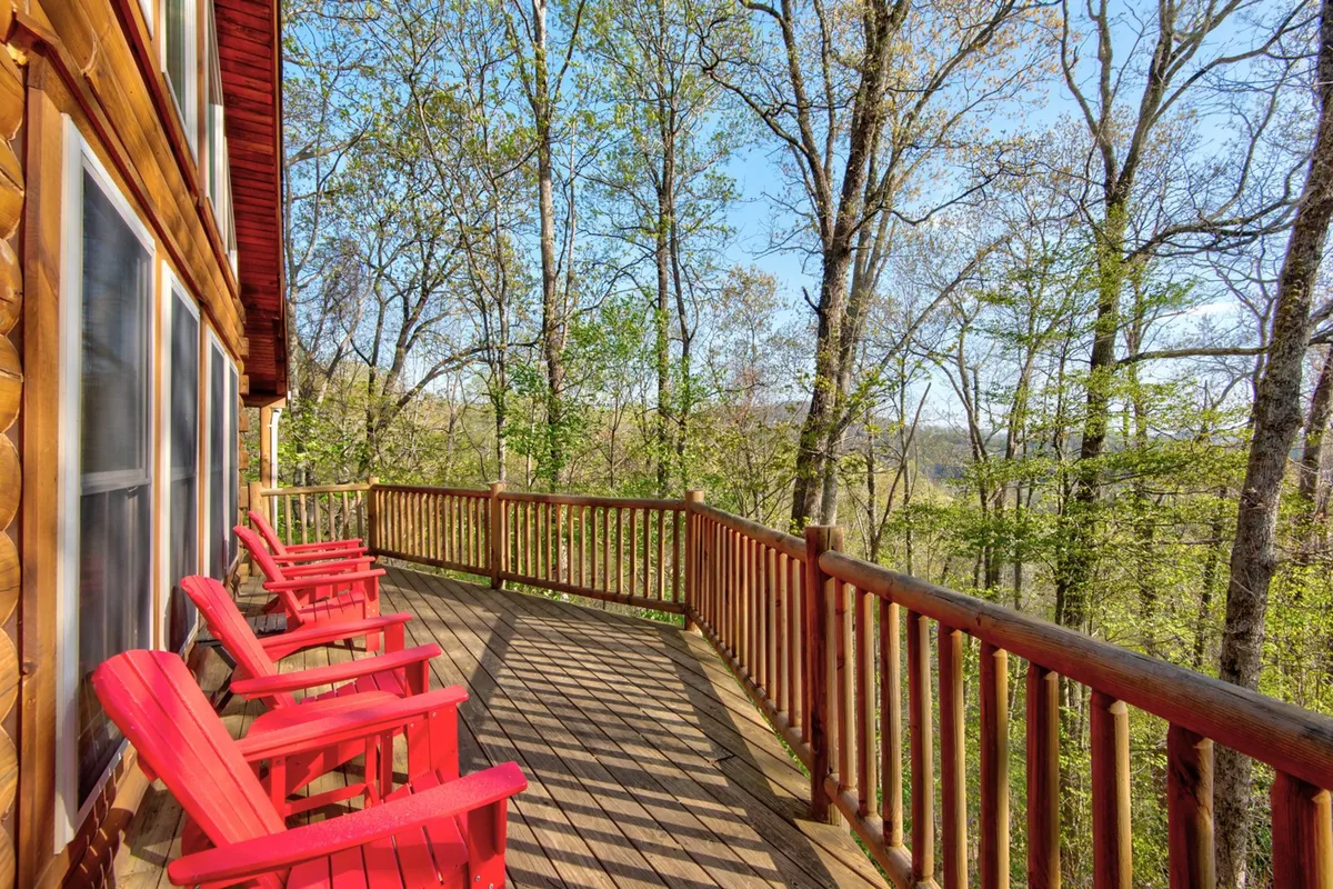 This exterior image shows two red Adirondack chairs set on a wooden deck, overlooking a peaceful natural landscape. The scene invites relaxation while taking in the tranquil surroundings. The deck’s wooden railing frames the view, and the seating faces outward toward mountains or woods, evoking a sense of privacy and immersion in nature.