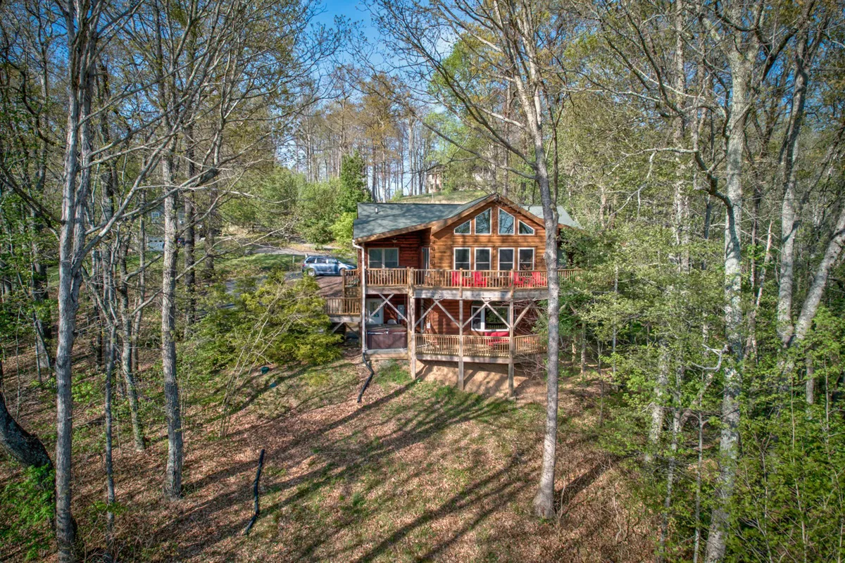 A cozy wooden cabin with a balcony featuring two bright red chairs, surrounded by lush trees. The setting highlights the connection between the lodge and the natural landscape, with the balcony offering a prime vantage for enjoying the outdoors.