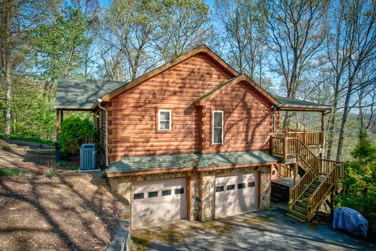 This image shows the exterior of Chestnut Lodge, highlighting its classic log cabin structure, a spacious wooden deck perfect for gatherings, and the prominent two-car garage that provides practical storage for outdoor gear. The lodge is set amidst lush greenery, emphasizing its proximity to nature and outdoor adventure.