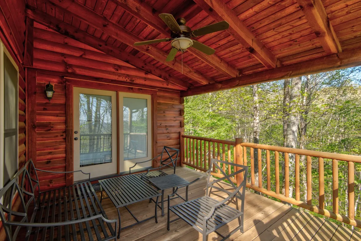 A tranquil deck space with a wooden railing, metal furniture, ceiling fan, and large glass doors opening to the interior. The deck is oriented for stargazing, wildlife watching, and entertaining, blending indoor comfort with outdoor experiences.